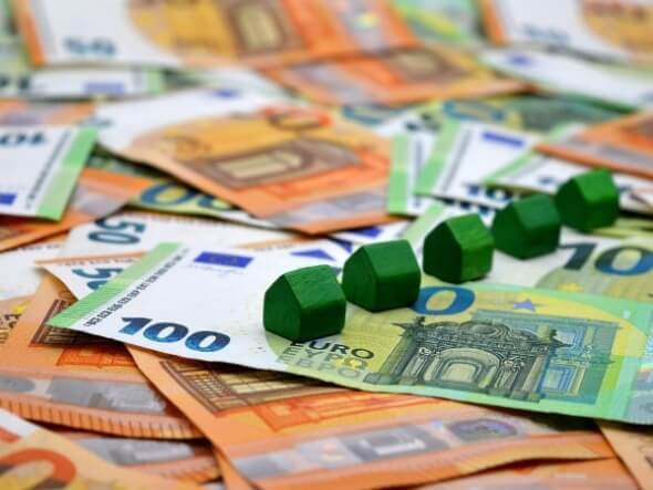 Mehrere 50- und 100-Euro-Scheine, auf denen grüne Miniatur-Häuser stehen.