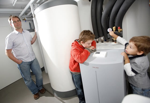 Vater und zwei Kinder schauen sich die Wärmepumpe im Keller mal genauer an
