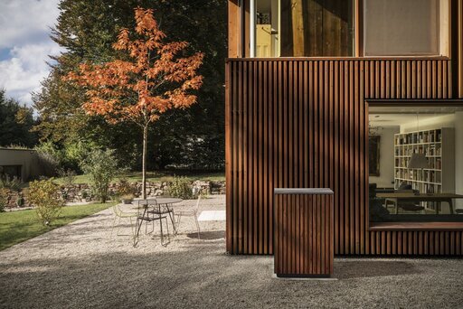 Die Terrasse einer modernen Immobilie mit großen Glasflächen und Holzfassade. Passend dazu erhielt die freistehende Wärmepumpe von Glen Dimplex Thermal Solutions eine perfekt zur Fassade passende Holzhülle.