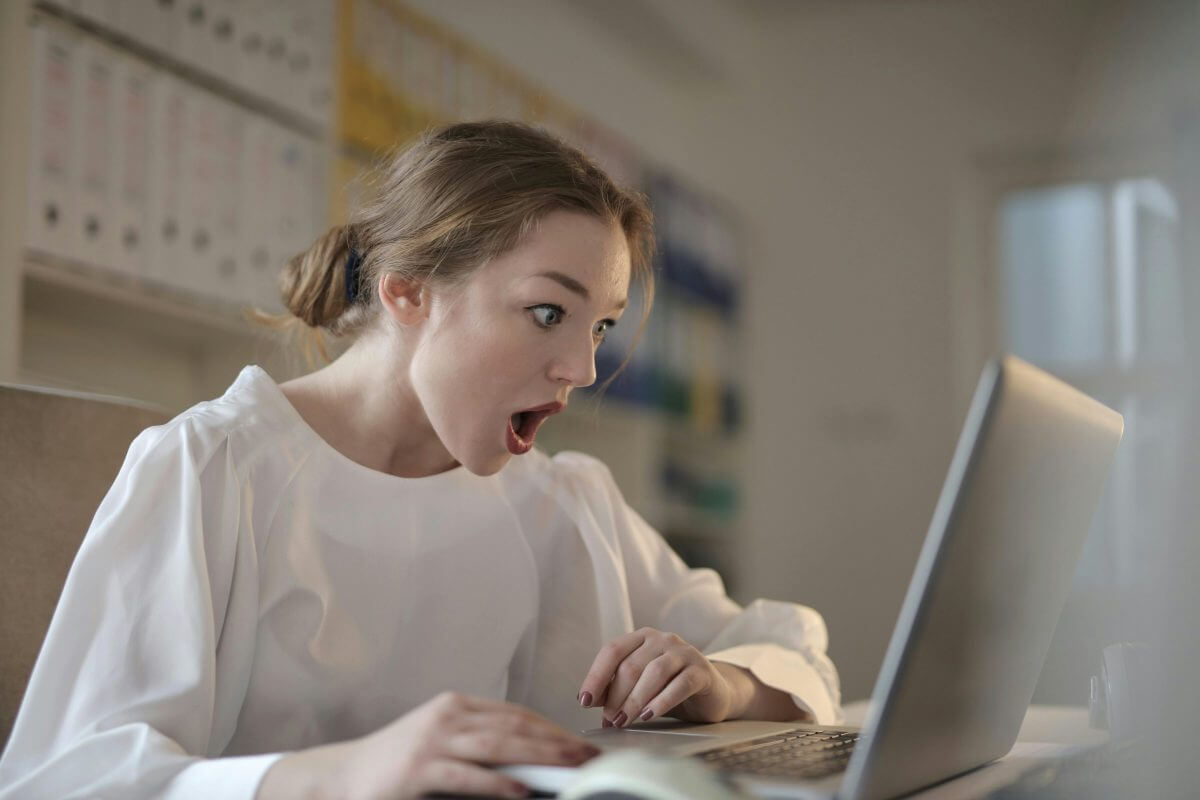 Junge Frau sitzt überrascht vor dem Laptop.