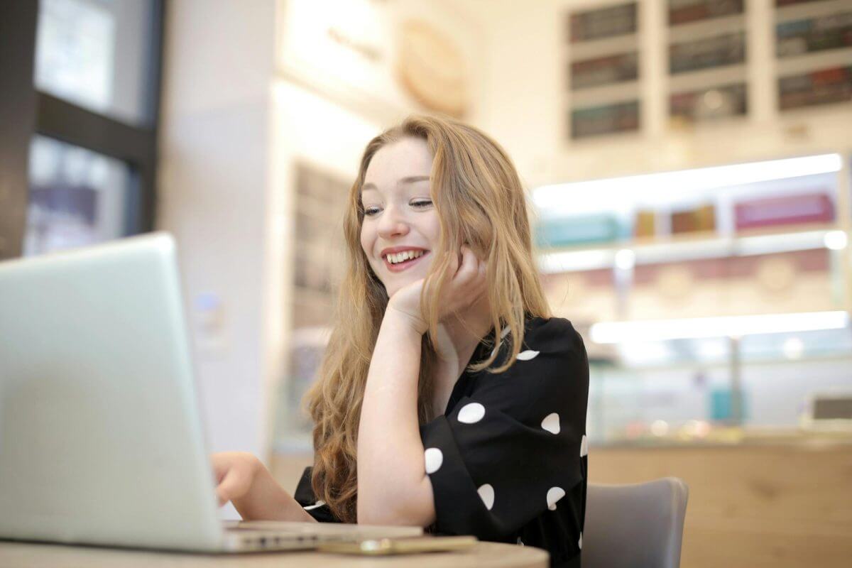 Eine junge Frau sitzt lachend vor dem Laptop.