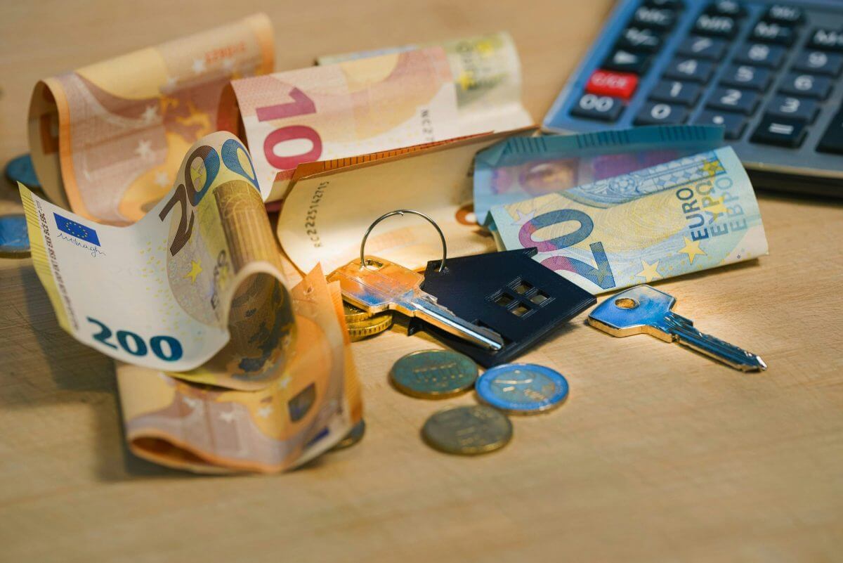 Geldscheine, Münzen, ein Schlüsselbund mit Hausanhänger und ein Taschenrechner auf einem Tisch.