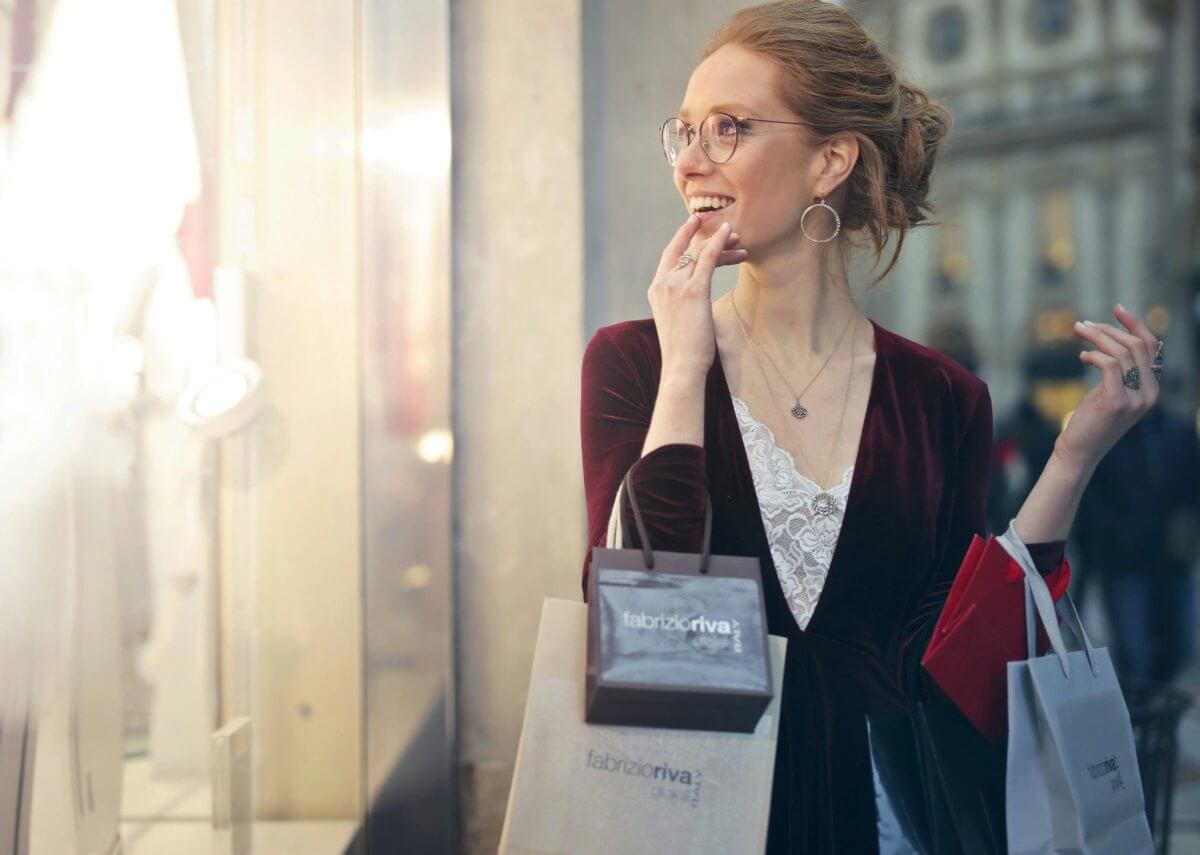 Eine mit Einkaufstüten beladene junge Frau freut sich an den Auslagen eines Schaufensters.