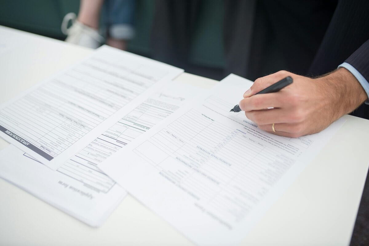 Ein Mann unterschreibt Unterlagen – Symbolbild für den bürokratischen Aufwand bei der Genehmigung von Aufstockungen.