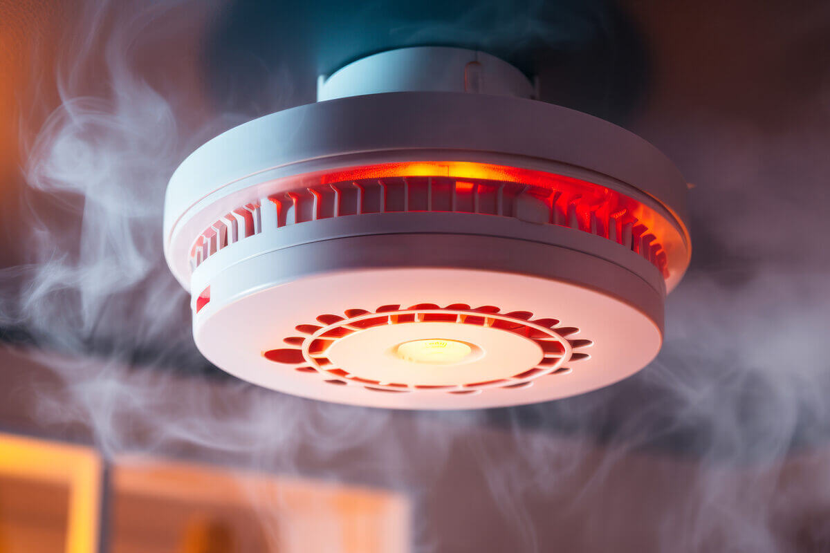 Aktiver smarter Rauchmelder mit rotem Warnlicht und Rauchentwicklung.
