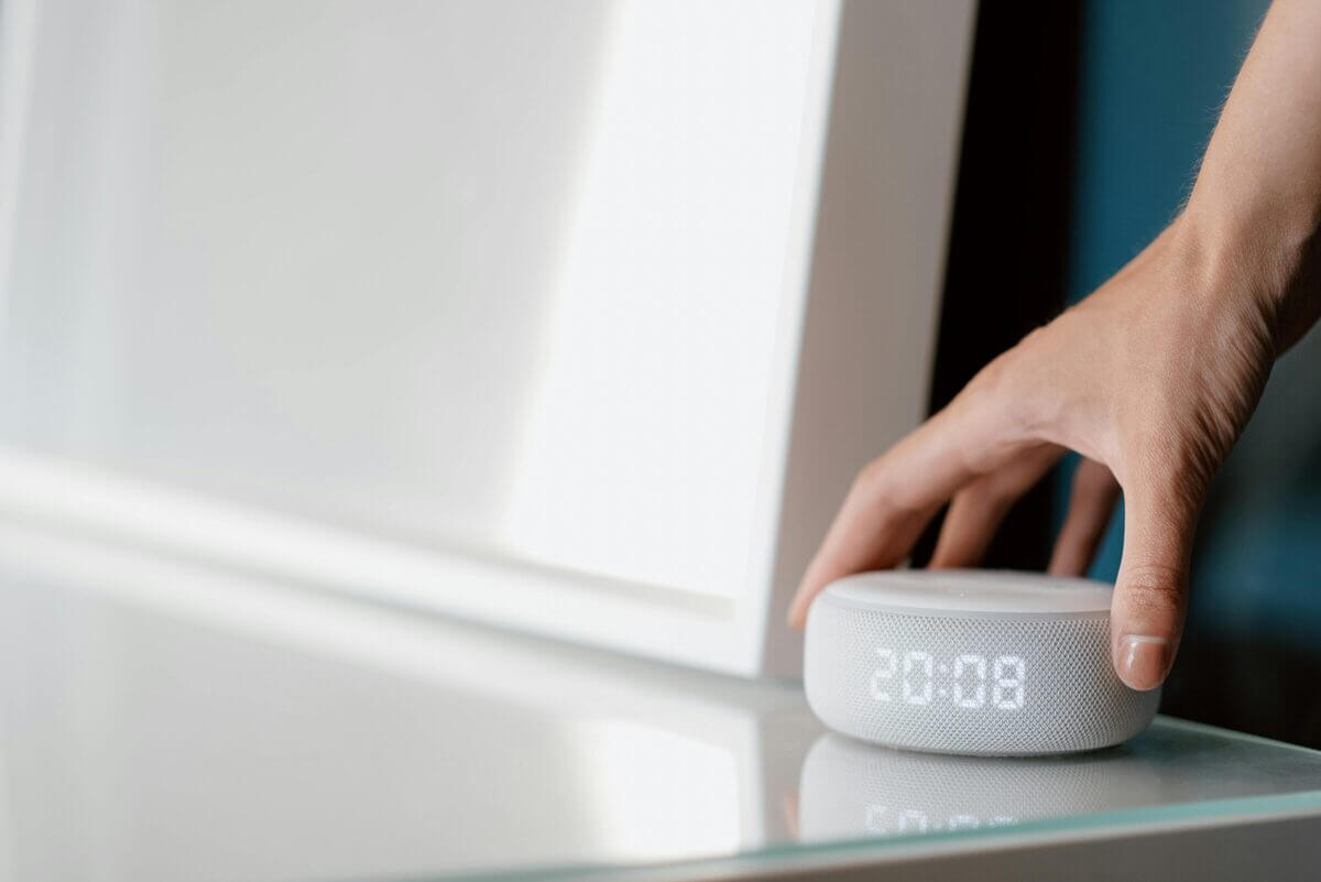 Hand auf smartem Lautsprecher mit digitaler Uhranzeige.