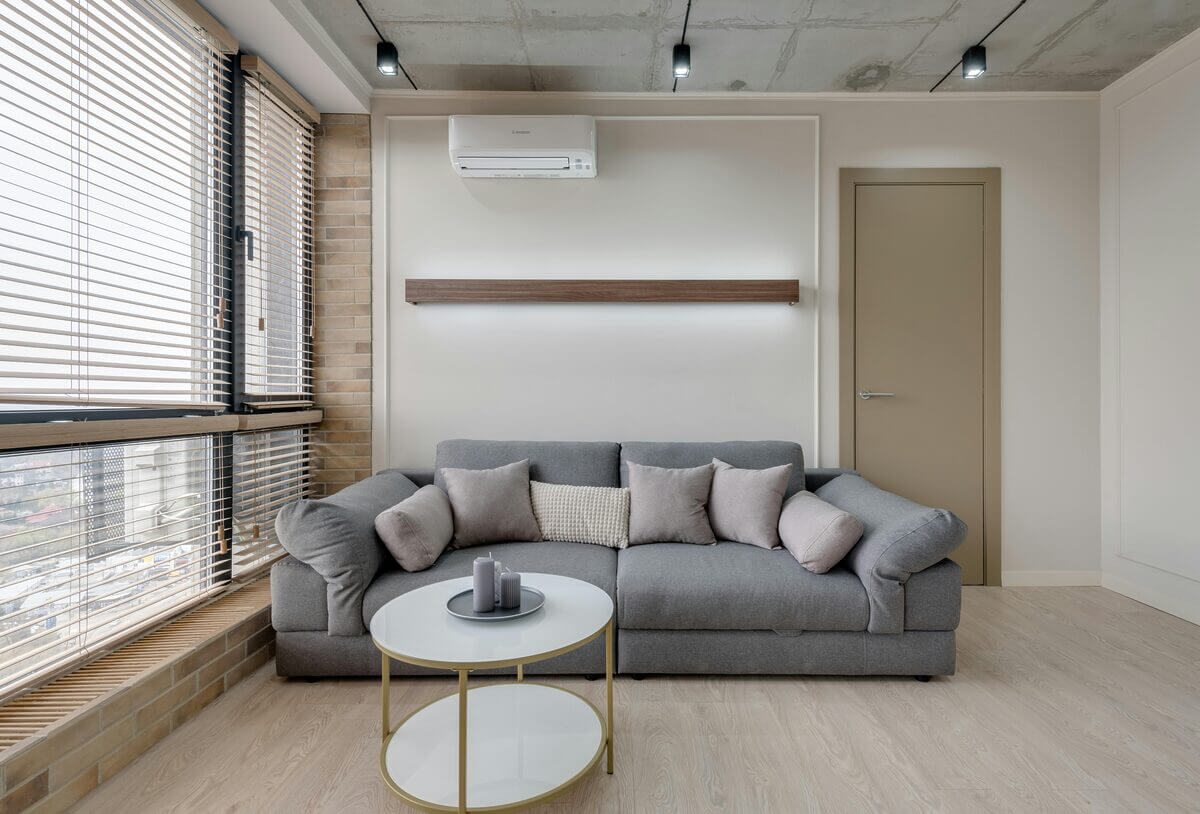 Wohnzimmer mit grauem Sofa und weißer Split-Klimaanlage an der Wand montiert.