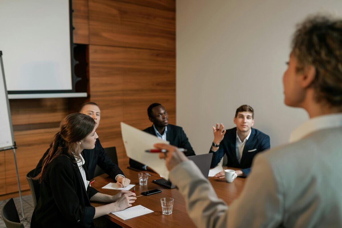 Weibliche Person hält eine Präsentation vor einer kleinen Gruppe im modernen Konferenzraum.